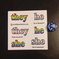 rainbow she, he, they and pink/blue/white she, he, they stickers on a sheet with a d20 for size